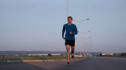 The guy runs along the road at sunset. Front view 库存影片 64494997