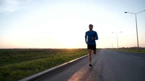 The guy runs along the road at sunset. Front view 库存影片 64495287