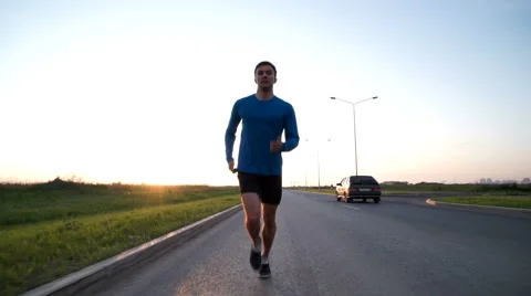 The guy runs along the road at sunset. Front view Stock Footage 64495493