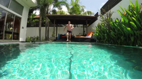 Guy runs up and jumps into the pool Video stock 50863900