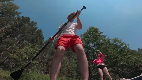  A guy is sailing on a SUP board, surrounded by two girls. SUP board on a forest Stock Footage 278508403
