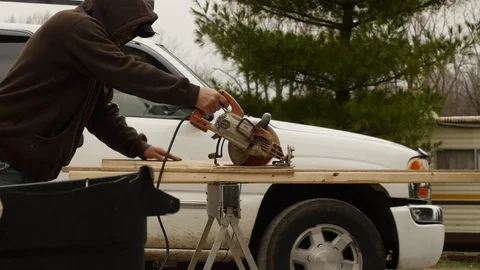 Guy Sawing Wood in Front of White Pick-Up Truck Stockbeeldmateriaal 104890655
