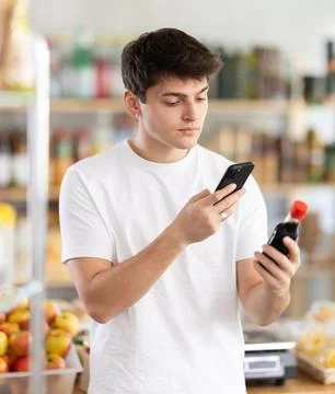 Guy scanning barcode on soy sauce using phone in food store Stock Photos
