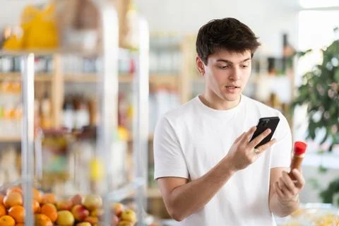 Guy scanning QR code on bottle of red pepper with phone Stock-Fotos