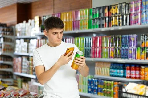 Guy scans bar code from label of an aluminum can with drink in grocery 写真素材
