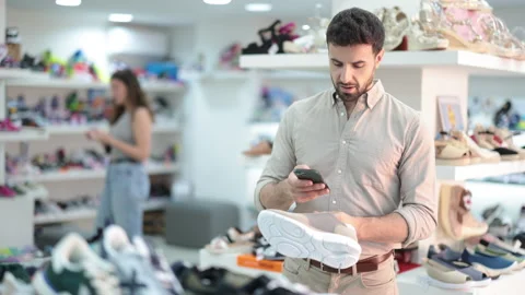 Guy scans QR code on the label of new sneakers in a shoe store Vídeo Stock 344776116