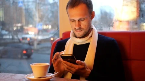 Guy with a scarf looks into the phone while sitting at the table 動画素材 102545185