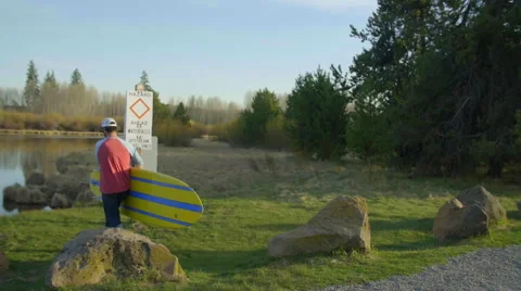 Guy sets down paddle board by water Stock Footage 63385705