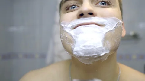 The guy shaves with an electric razor in the bathroom. The guy is looking in the Stock Footage 120359449