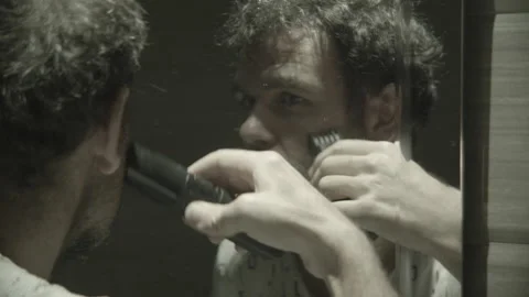 The guy shaves his beard with a trimmer in front of the bathroom mirror Stock Footage 131465065