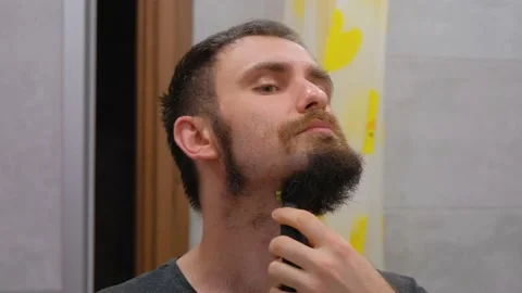 The guy shaves off his big beard. Young guy shaves his beard at home. A man Stock Footage 231495189