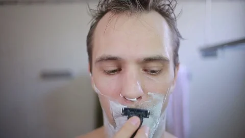 Guy shaving off his beard with a razor in the bathroom Stock Footage 73412988