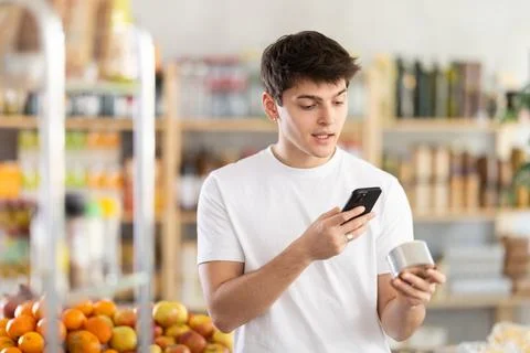 Guy shopper scanning QR code on tin can label in grocery department of Photos