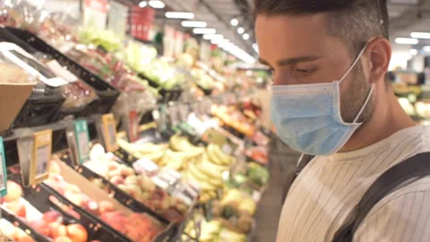 A guy shopping, buying fruit in a supermarket. Wearing a protective medical mask Stock Footage