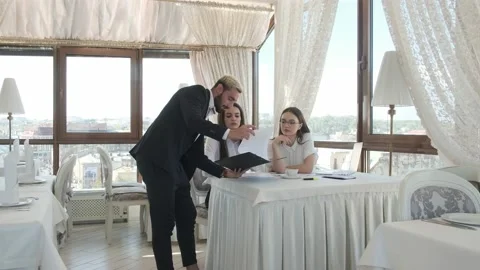 Guy shows the documents to the girls sitting at the table Stock Footage 130913067