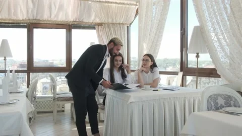 Guy shows the documents to the girls sitting at the table Video stock 130913278