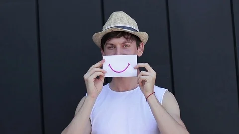The guy shows emotions with the help of a smiley on paper Stock Footage 78743021