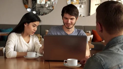 Guy shows something on laptop to his friend at the cafe Stock Footage 311992022