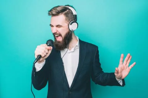Guy is singing in microphone. Also he has the headphones on his hand. He is Stock Photos