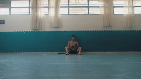 Guy sits alone in dojo wrapping wrists Stock Footage 275431019