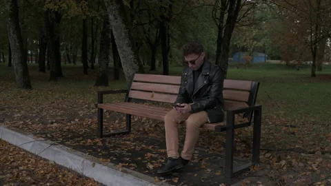 The guy sits in the autumn park Vidéo 219229559