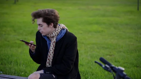 A guy sits on a bench and records an audio message,puts the phone in the pocket. Vidéo 201075950