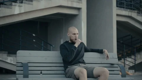 The guy sits on a bench and vaping in the evening on the street Stockbeeldmateriaal 85600174