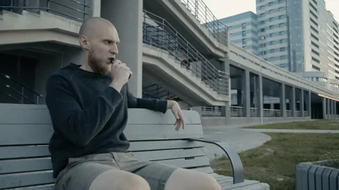 The guy sits on a bench and vaping in the evening on the street Stockbeeldmateriaal 85611220