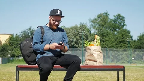 The guy sits on a bench with a package of products Stock Footage 113475005