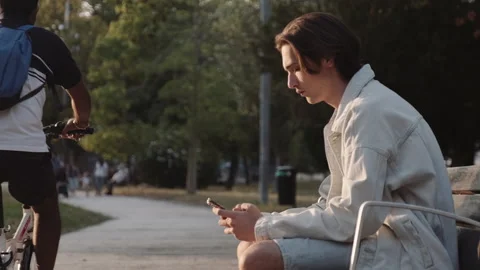 Guy sits on the bench at park and typing a text message on a mobile phone. Stock Footage 201610114