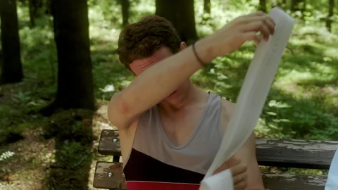 A guy sits on a bench in the woods and pulls out a long receipt tape. Stock Footage 197480248