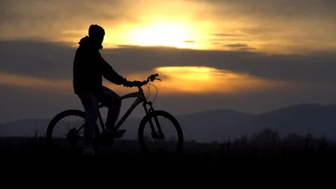 The guy sits on a bicycle, looks in different directions, a wonderful sunset Stock Footage 122237300