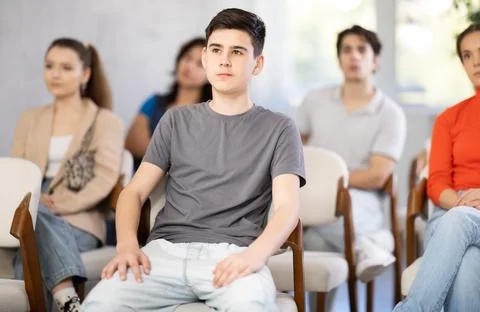 Guy sits in the classroom against the background of other students and listens Stock Photos