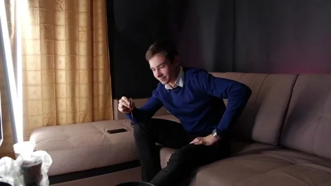 The guy sits on the couch and holds a live worm in his hand. Before eating a Stock Footage 152034900