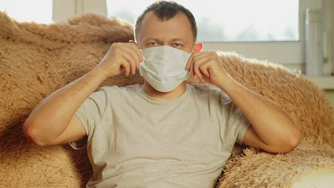 Guy sits on the couch, puts on a medical mask and leaves Stock Footage 129690939