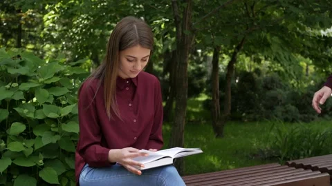 A guy sits down on a bench to a girl with a book Stock Footage 134253757
