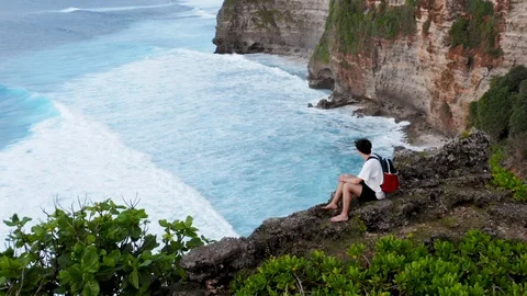 Guy sits on edge of cliff. Young boy coming to edge of cliff and sitting down Stock Footage 121951761