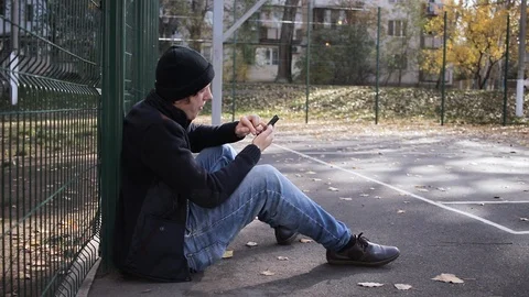 Guy sits on the ground in the park and talks on the phone Stock Footage 125088267