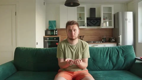 The guy sits at home on the couch and holds the text for insertion in his palms Stock-Footage 156905140