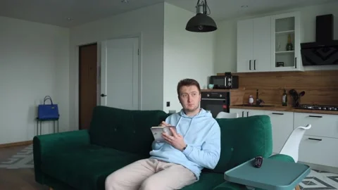 The guy sits at home on the couch, thinks, writes in a notebook, an idea arises Stock-Footage 154646641
