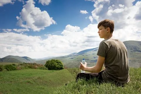 The guy sits on a mountain and drinks water from a bottle. mountain landscape. Stock Photos