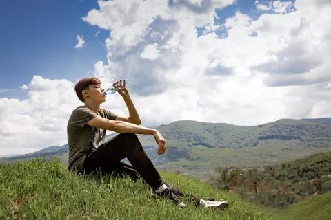 The guy sits on a mountain and drinks water from a bottle. mountain landscape. Stock Photos