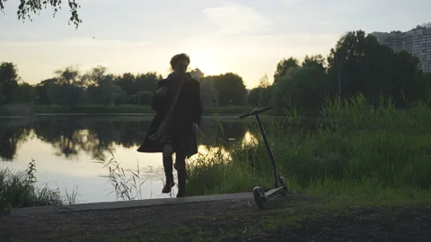 A guy sits near the lake, gets up, leaves on an electric scooter.Summer evening. Stock-Footage 201074227