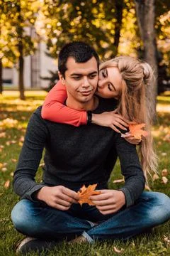 The guy sits in the park on the grass, and the girl in love hugs and kisses him Stock Photos