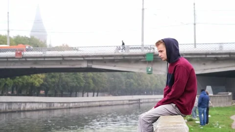 The guy sits by the river Vídeos de archivo 141527350