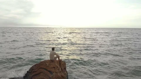 The guy sits on a rock and looks at the sunset Video stock 148292013