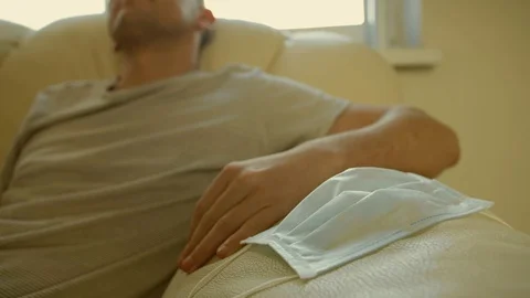 The guy sits on the sofa and removes his face mask Stock Footage 129438226
