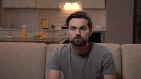 Guy sits on sofa and watches football game. He eats popcorn. Suddenly his team Stock-Footage 99739235