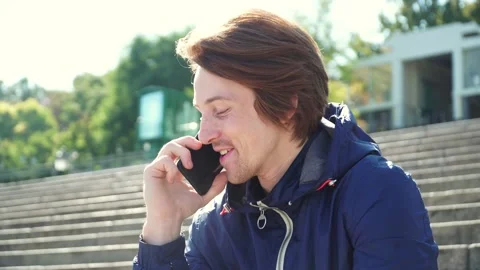 Guy sits on the steps and emotionally communicates on the phone in blue jacket Stock-Footage 163336255
