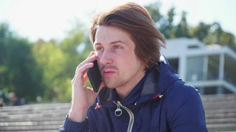Guy sits on the steps and emotionally communicates on the phone in blue jacket Stock-Footage 163336388